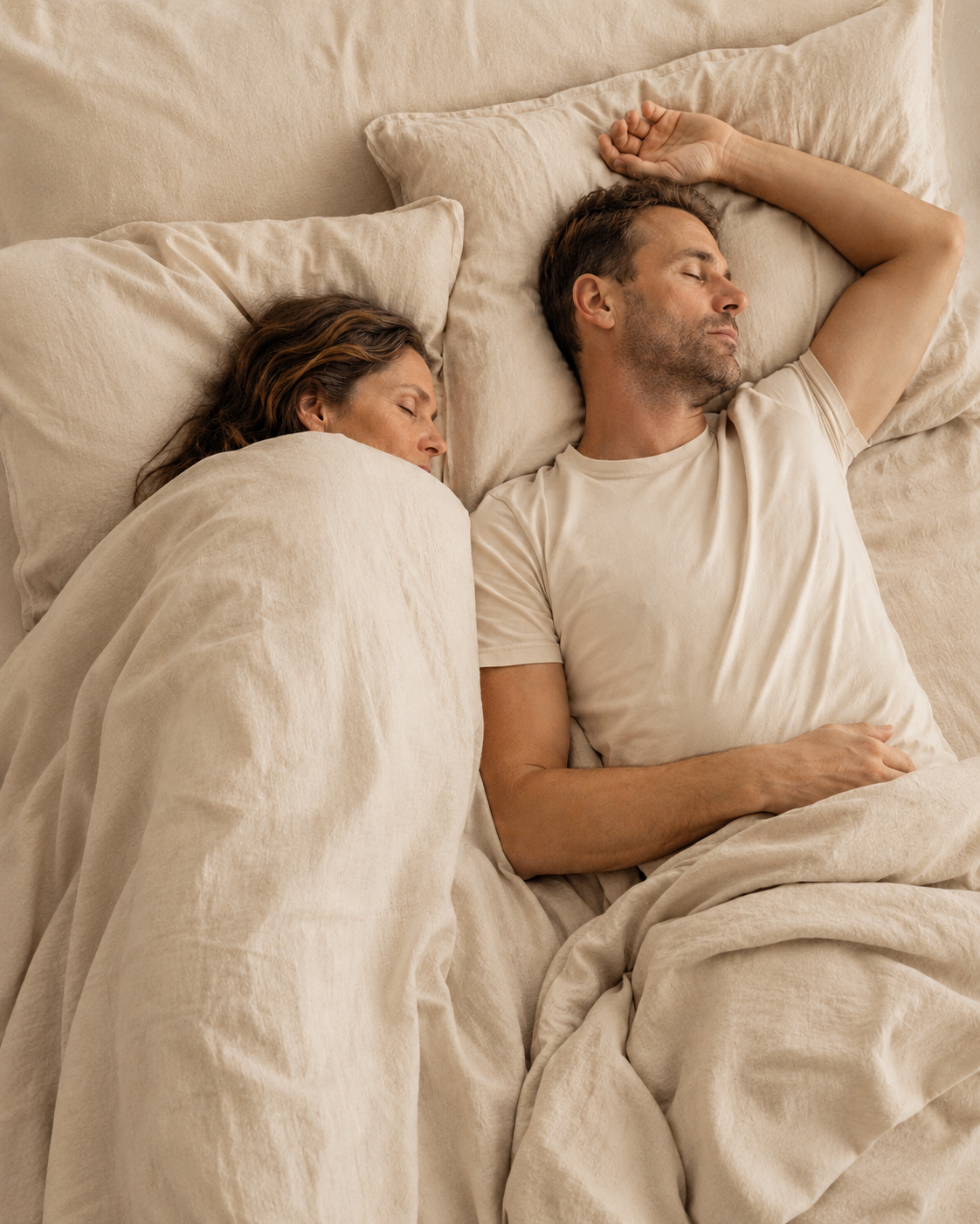 Par som sover i samme seng med hver sin dyne, kvinnen pakket inn og mannen med t-skjorte